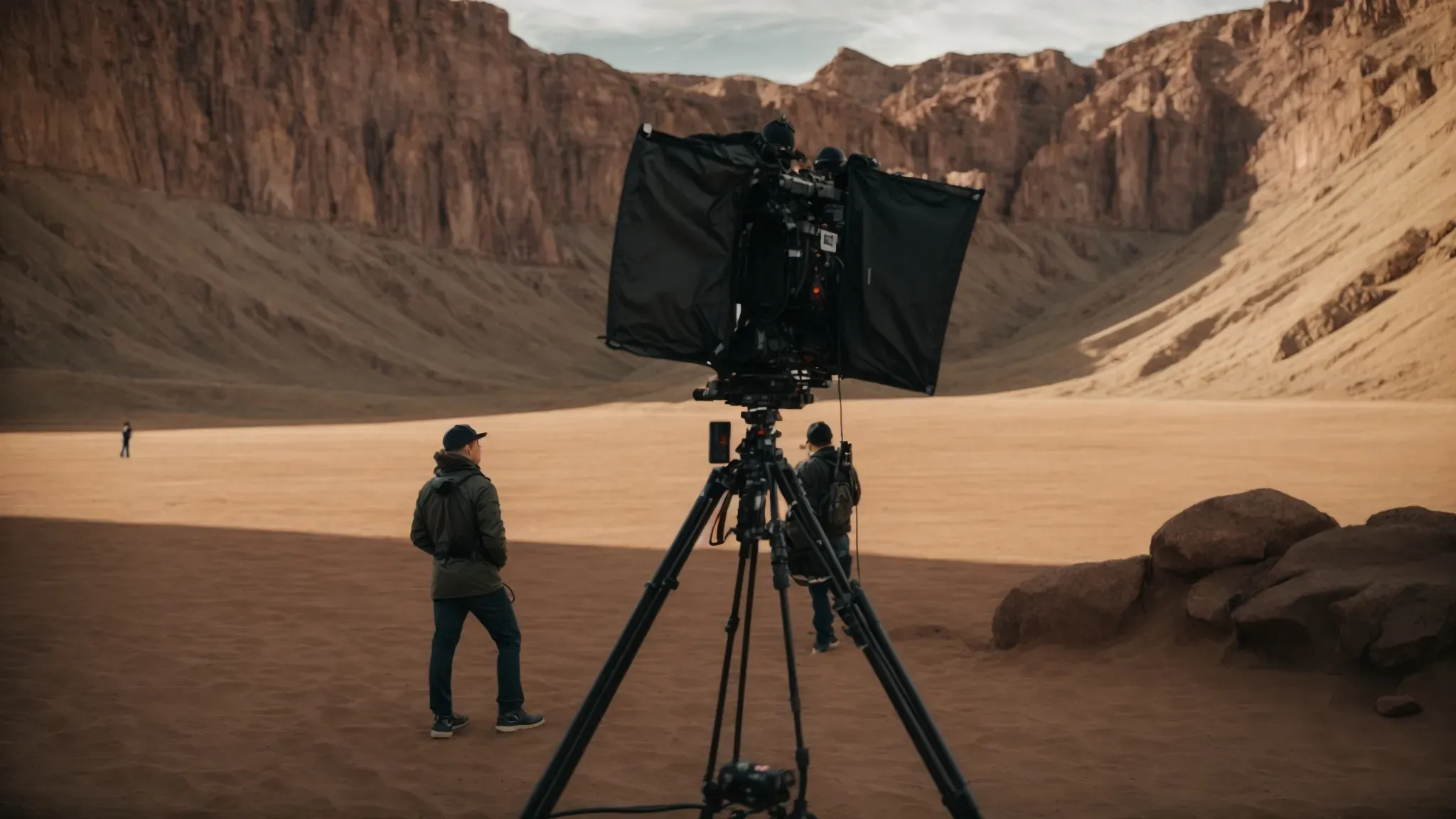 a director converses intently with a cinematographer on a film set, beneath the expansive canvas of a looming, otherworldly landscape.