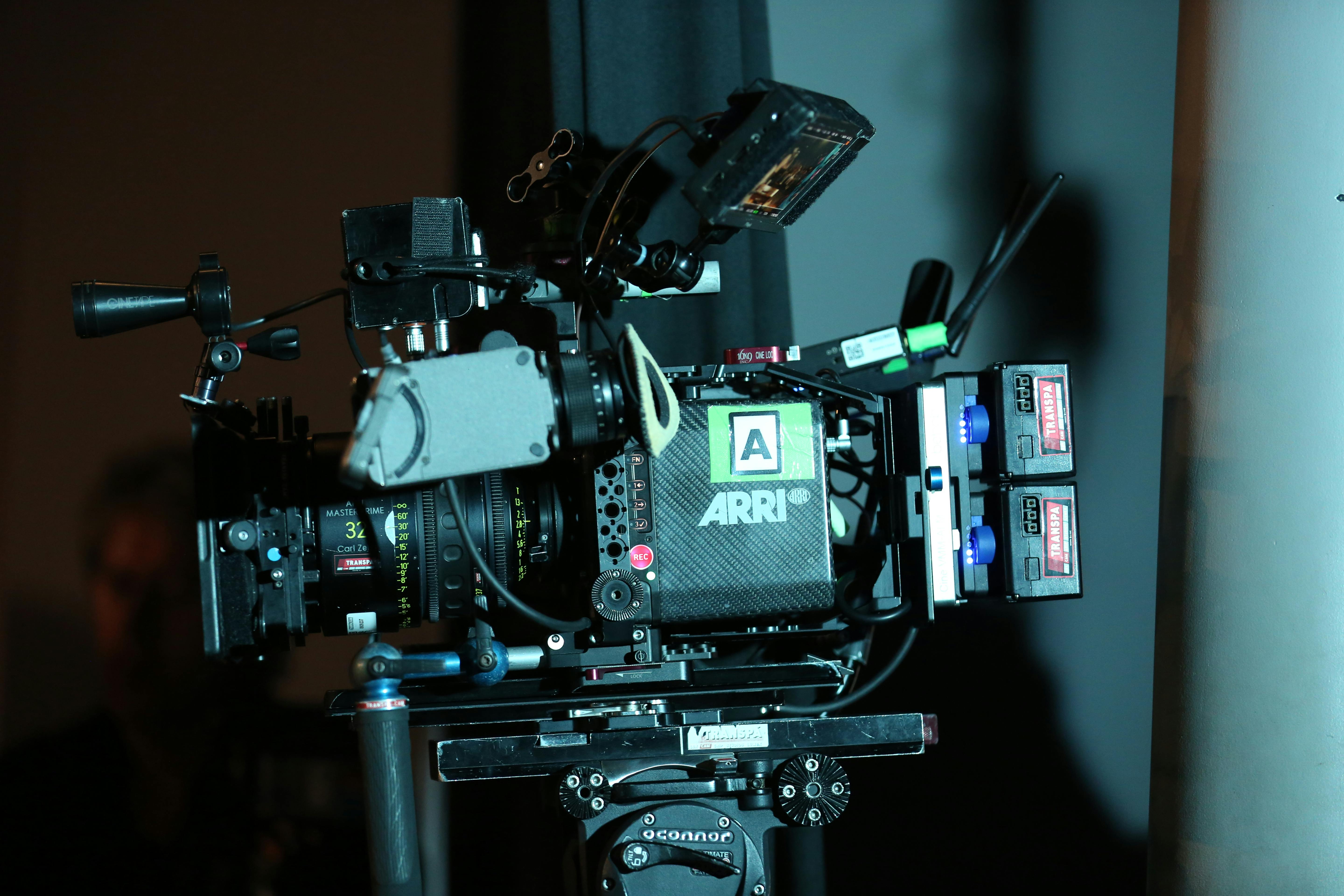 a director and cinematographer intently discussing in front of a camera setup, with a moodily lit film set in the background.