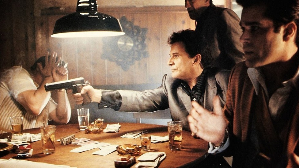 henry hill and his associates stride confidently through a dimly-lit restaurant, embodying the aura of mafia elegance.