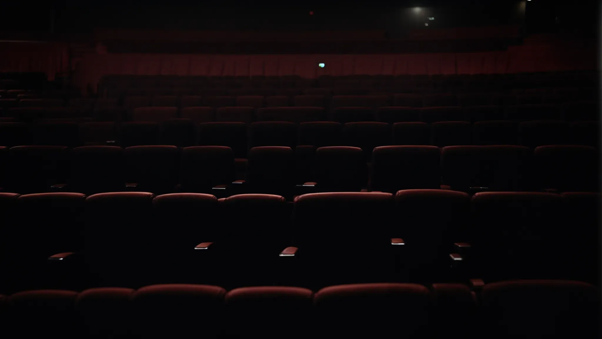 a wide cinema screen illuminates a dark theater, casting light on rows of empty seats.