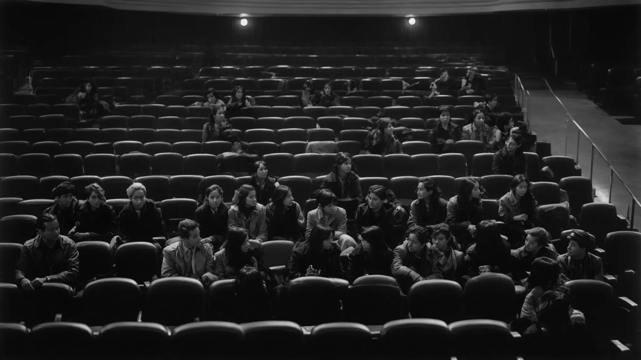 a group of people gathered in a vintage movie theater, discussing amid rows of empty seats.