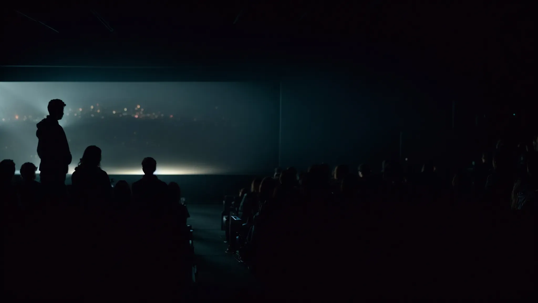 a dark cinema room illuminated by the bright screen showing the final scene of a movie, with a captivated audience in silhouette.