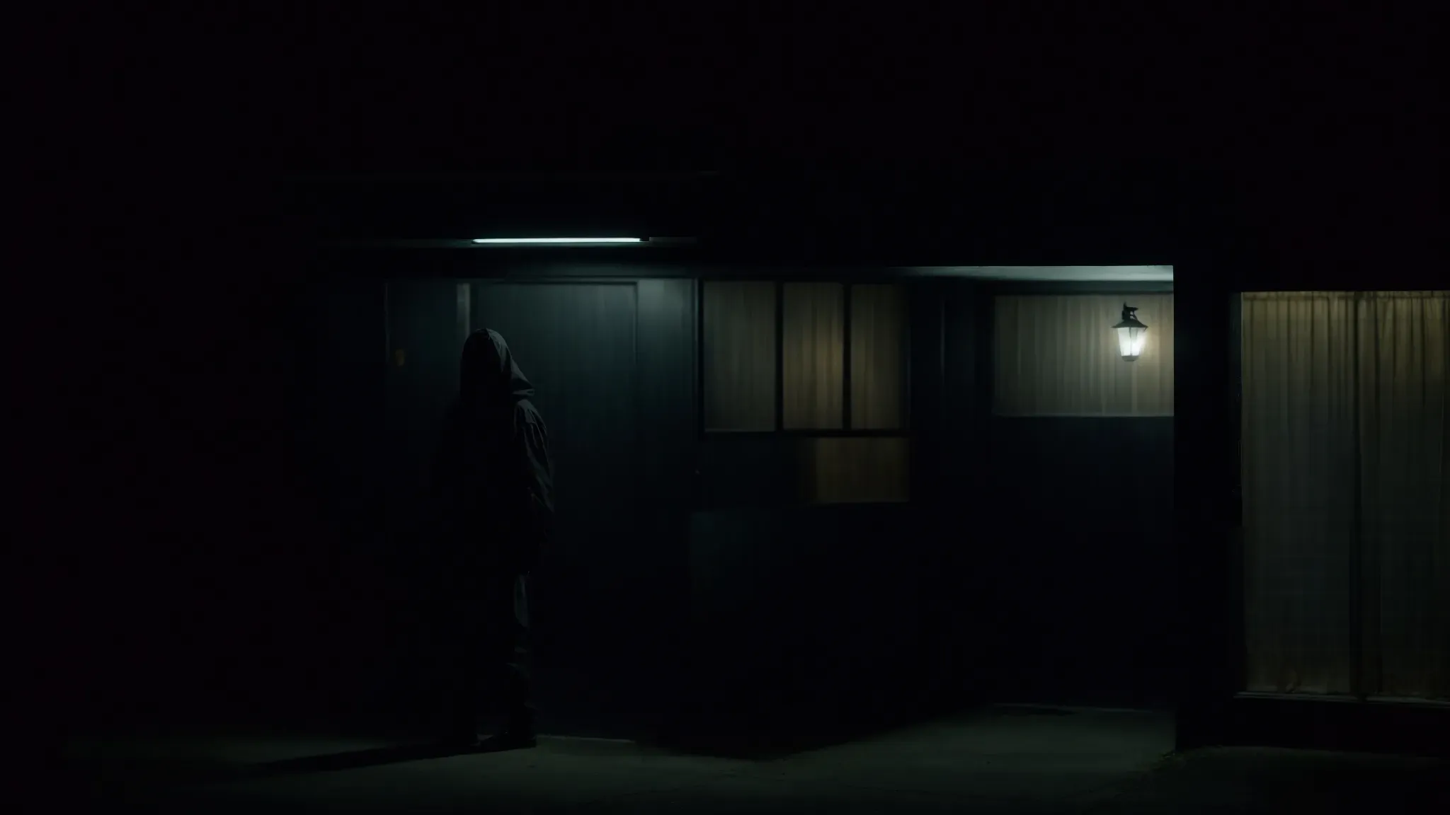 a shadowy figure stands ominously at the entrance of the bates motel under a flickering light.
