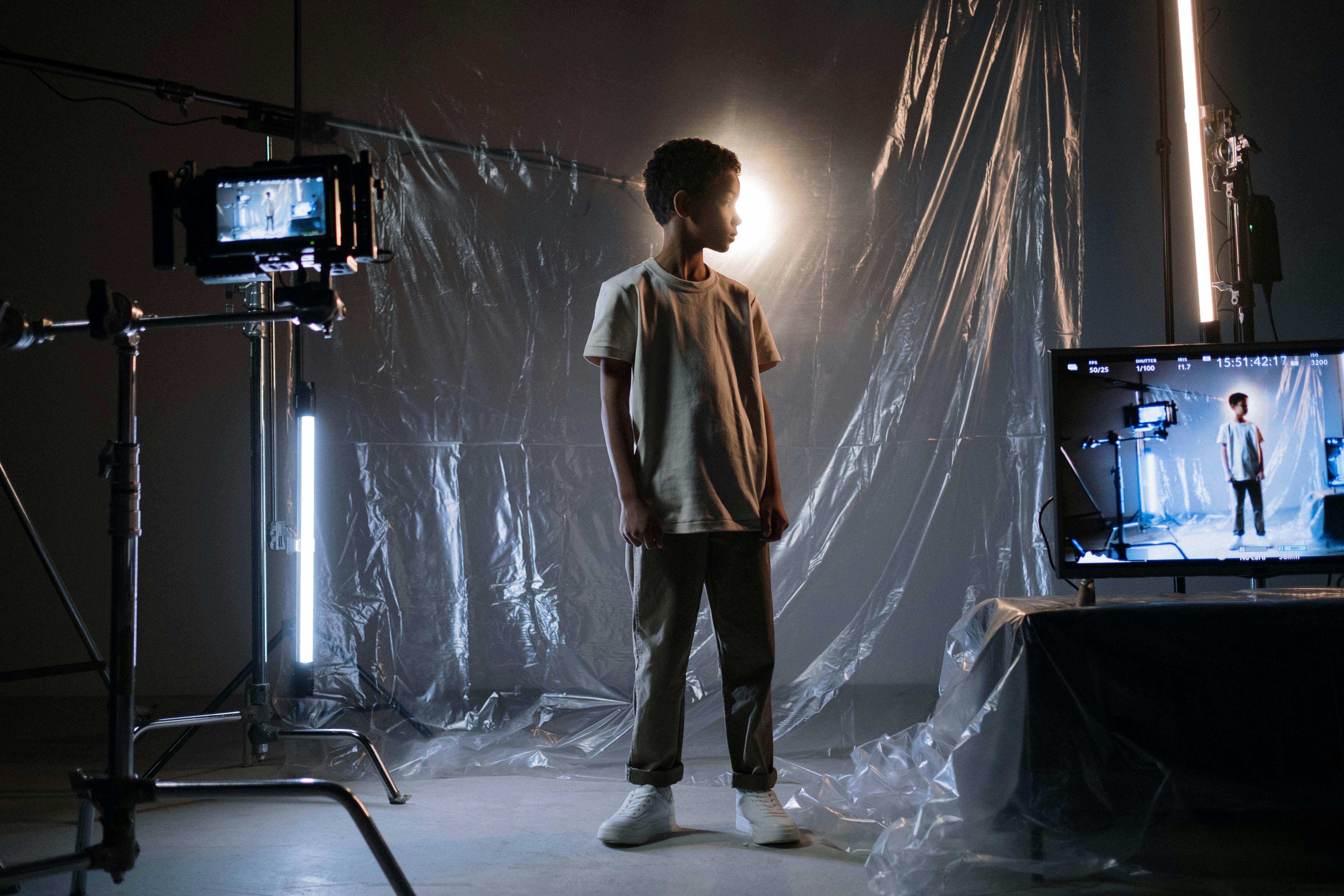 a young filmmaker stands contemplatively behind a camera set up in an indie film studio, surrounded by modest lighting equipment, facing an empty set awaiting transformation.
