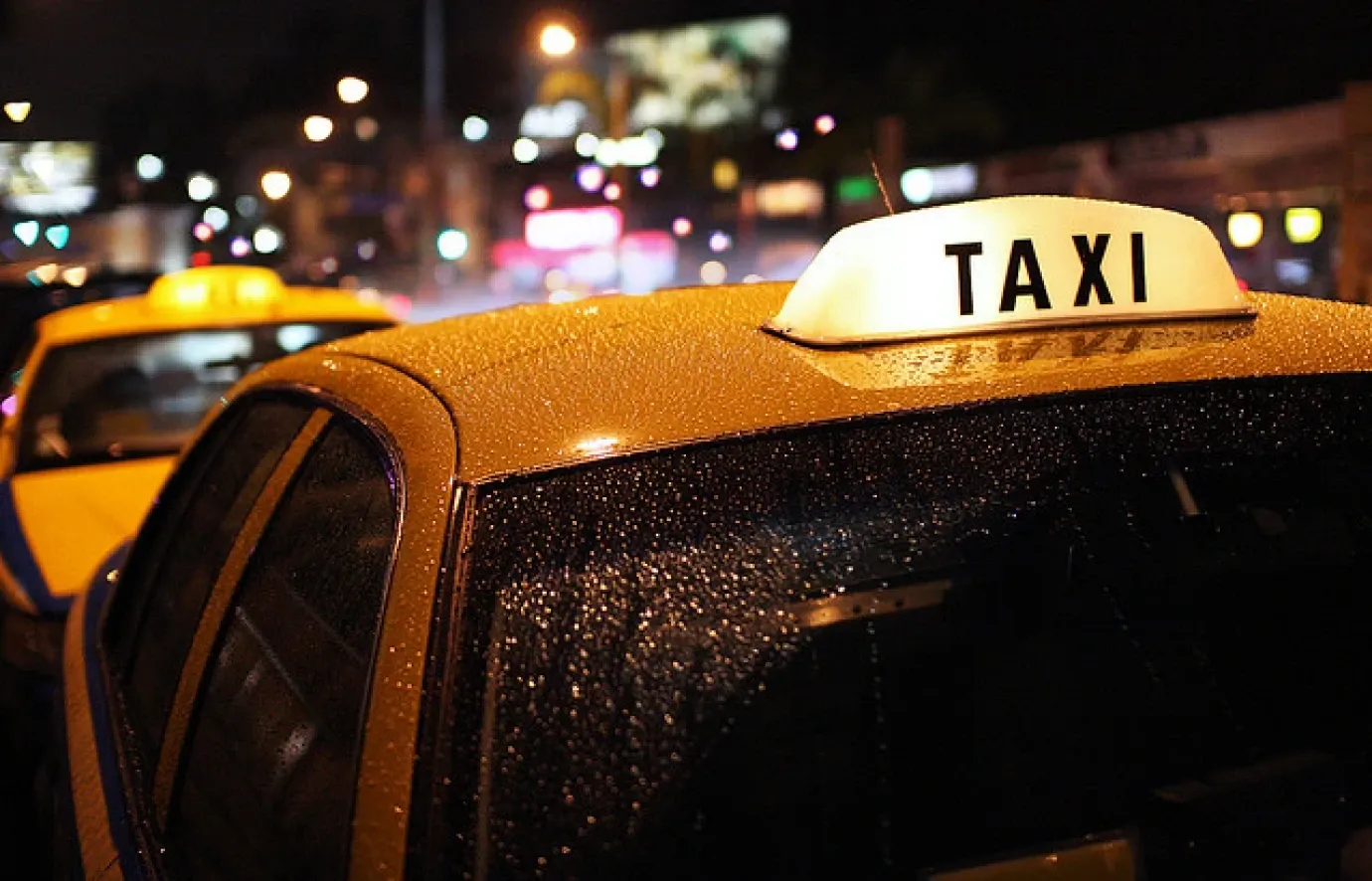 a lone taxi cruising through a neon-lit city street at night.